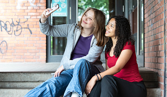 Foto von zwei jugendliche Mädchen, die auf einem Schulhof Selfies von sich machen