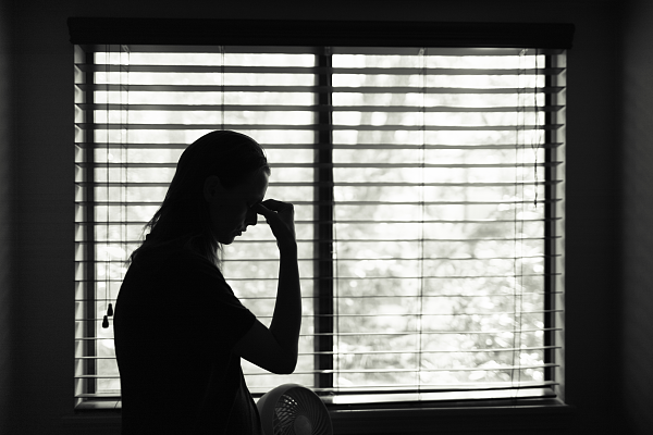 Es ist die Silhouette einer Frau vor einem Fenster mit Lamellenvorhang zu sehen.